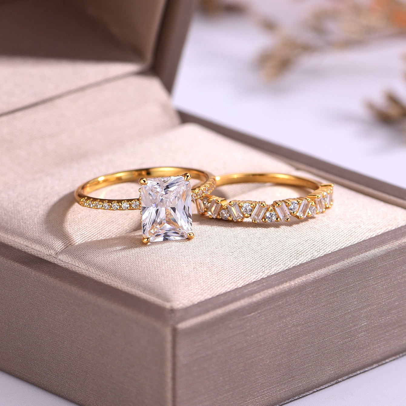 Two gold rings with diamond accents on a beige cushion inside a jewelry box.